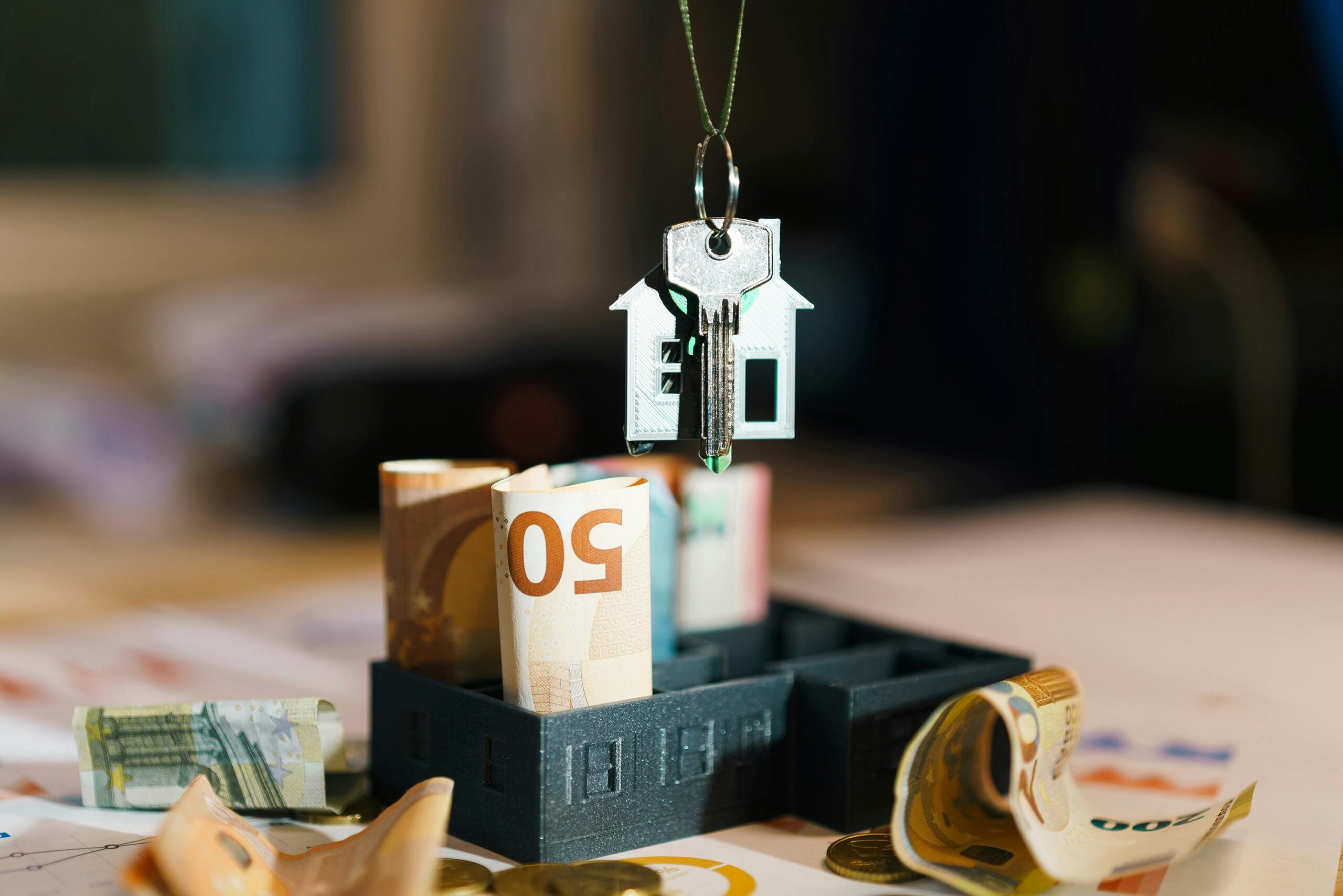 Selling Family Home image represents money on table with keychain of a silver house and house key dangling above the money